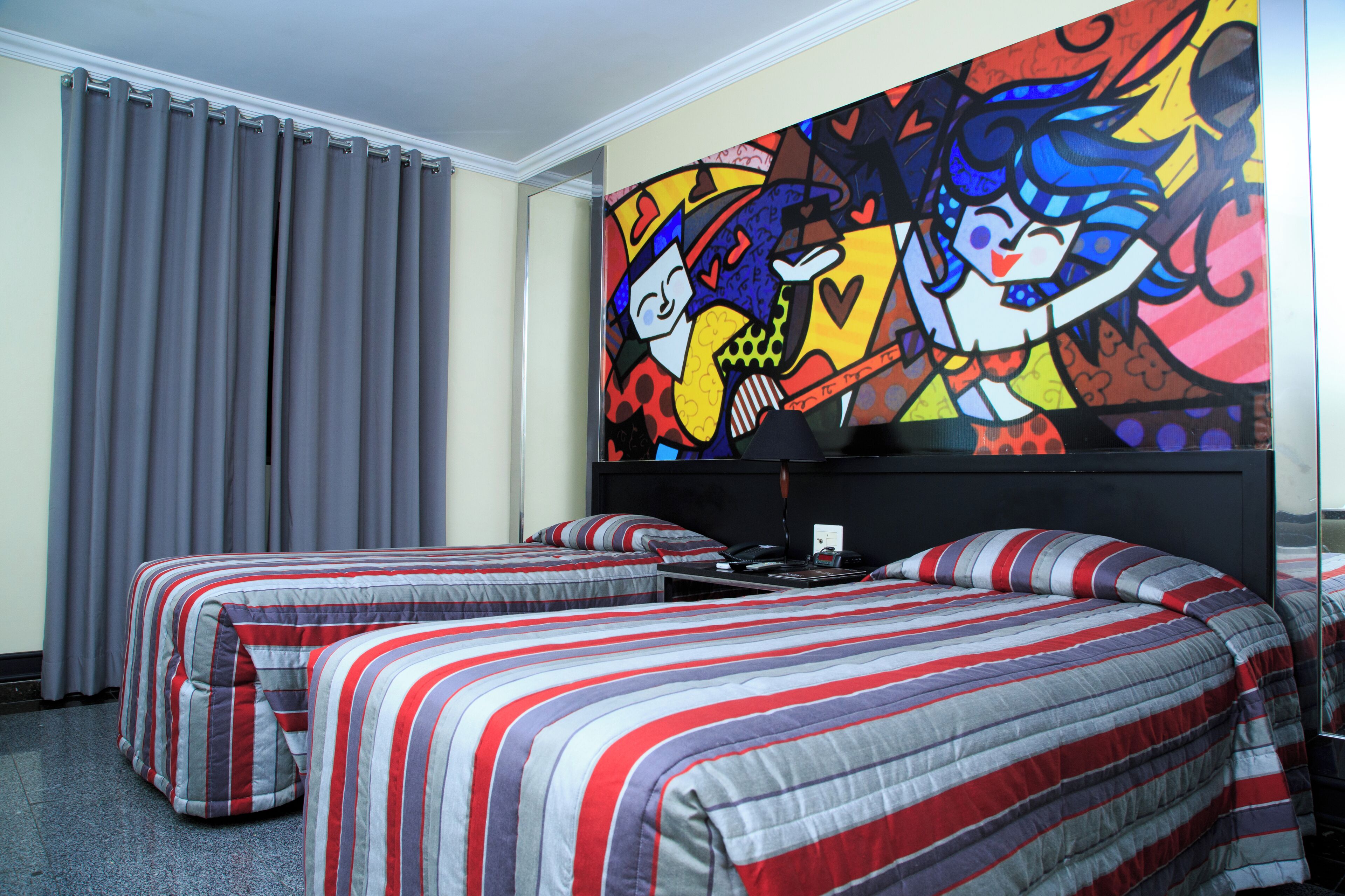 A hotel room with two beds, a large colorful artwork on the wall, and a window with curtains.
