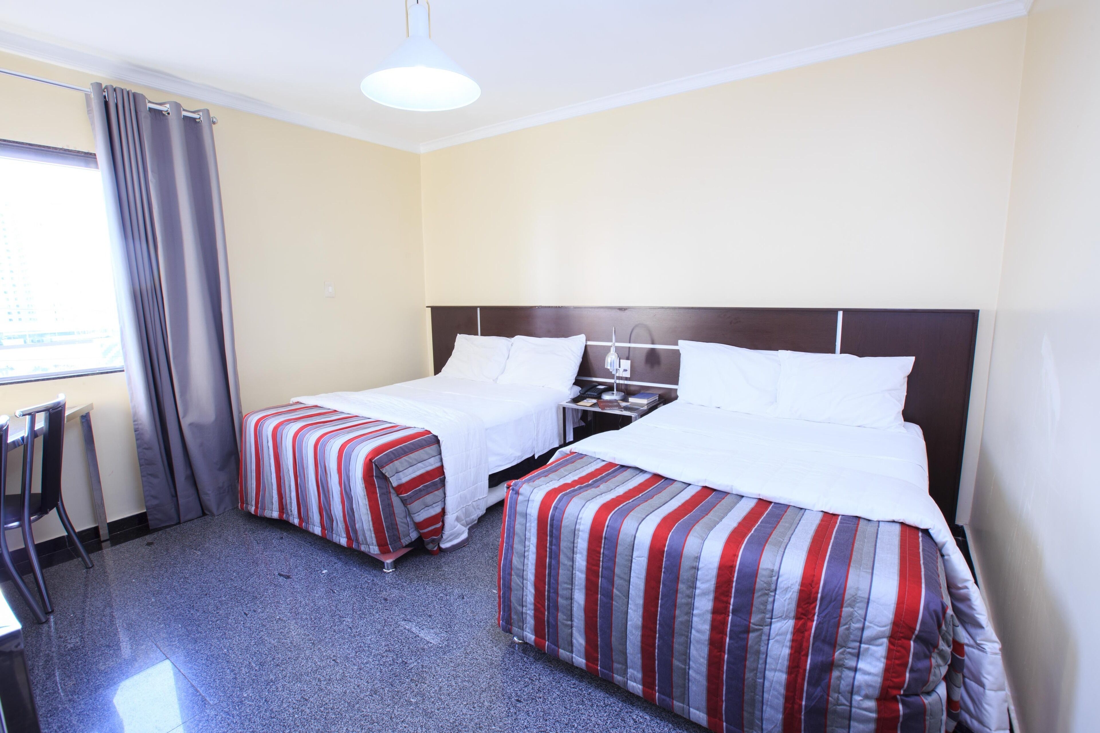 Habitación de hotel con dos camas individuales, un escritorio y una silla.