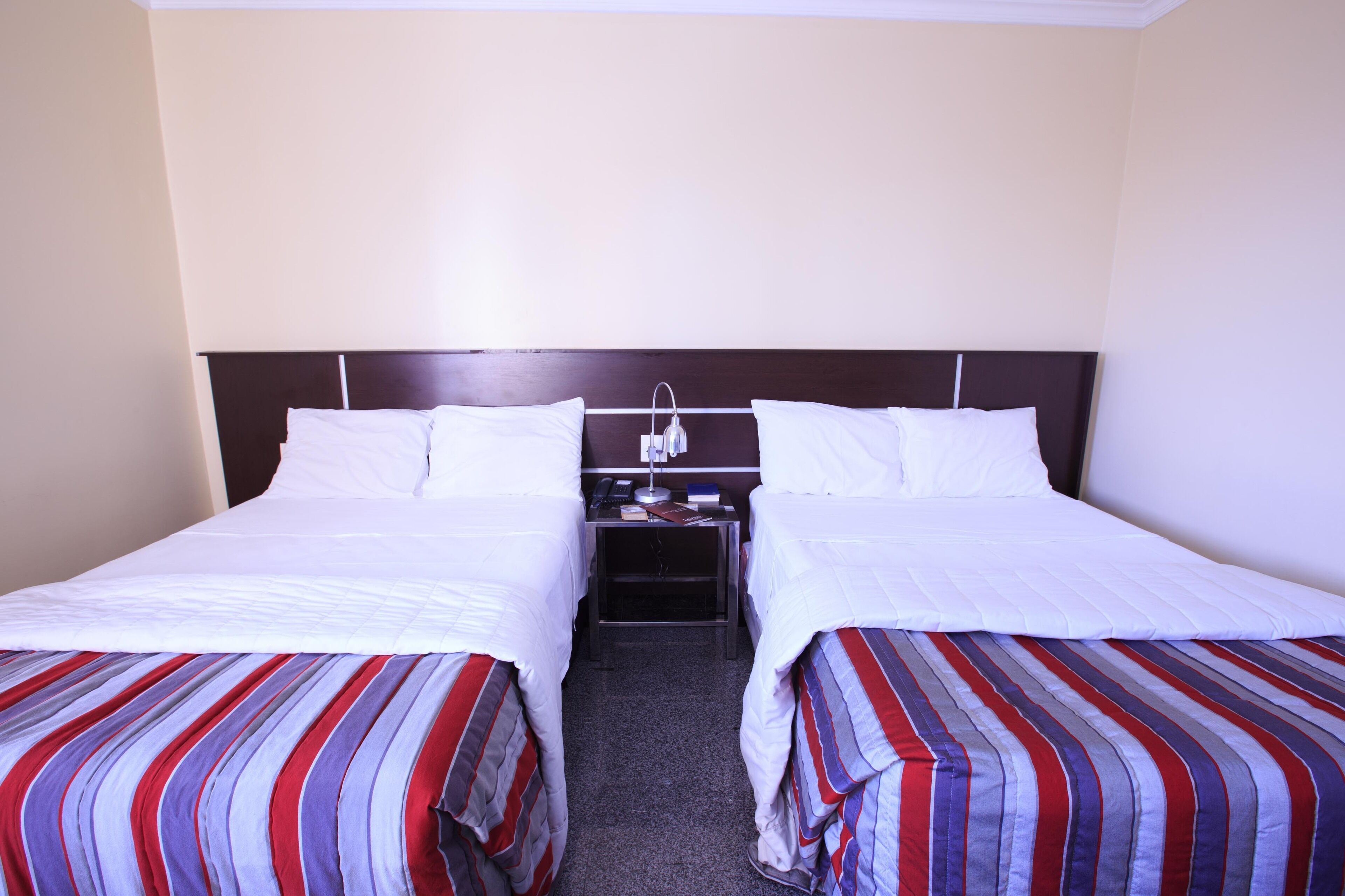 Una habitación de hotel con dos camas individuales, una mesita de noche con teléfono y lámpara, y una colcha a rayas.