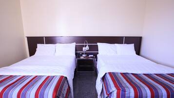 Una habitación de hotel con dos camas individuales, una mesita de noche con teléfono y lámpara, y una colcha a rayas.