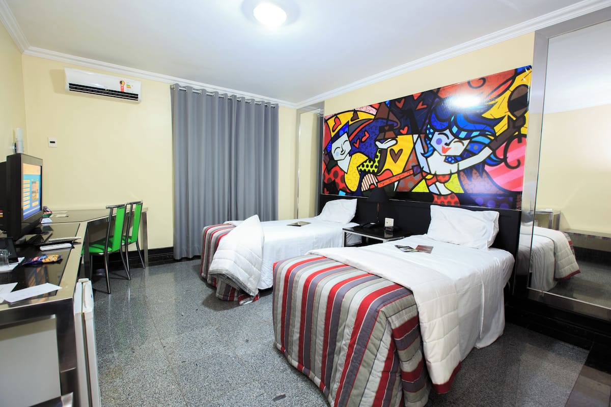 A hotel room with two beds, a desk with a computer, a chair, and a large colorful mural on the wall.