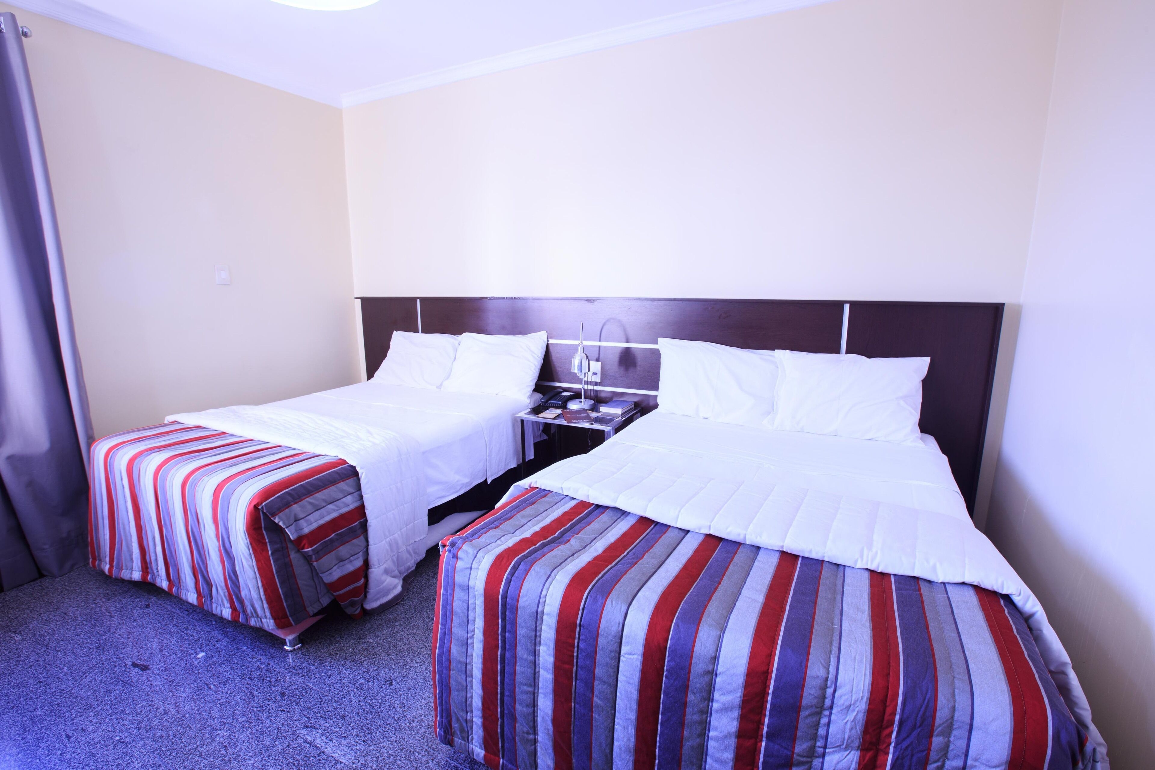 Una habitación de hotel con dos camas individuales, una mesita de noche y una lámpara.