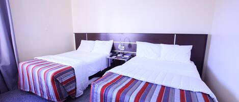 Una habitación de hotel con dos camas individuales, una mesita de noche y una lámpara.