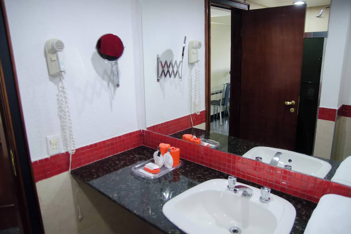 A bathroom with a sink, mirror, red-tiled backsplash, and a door.