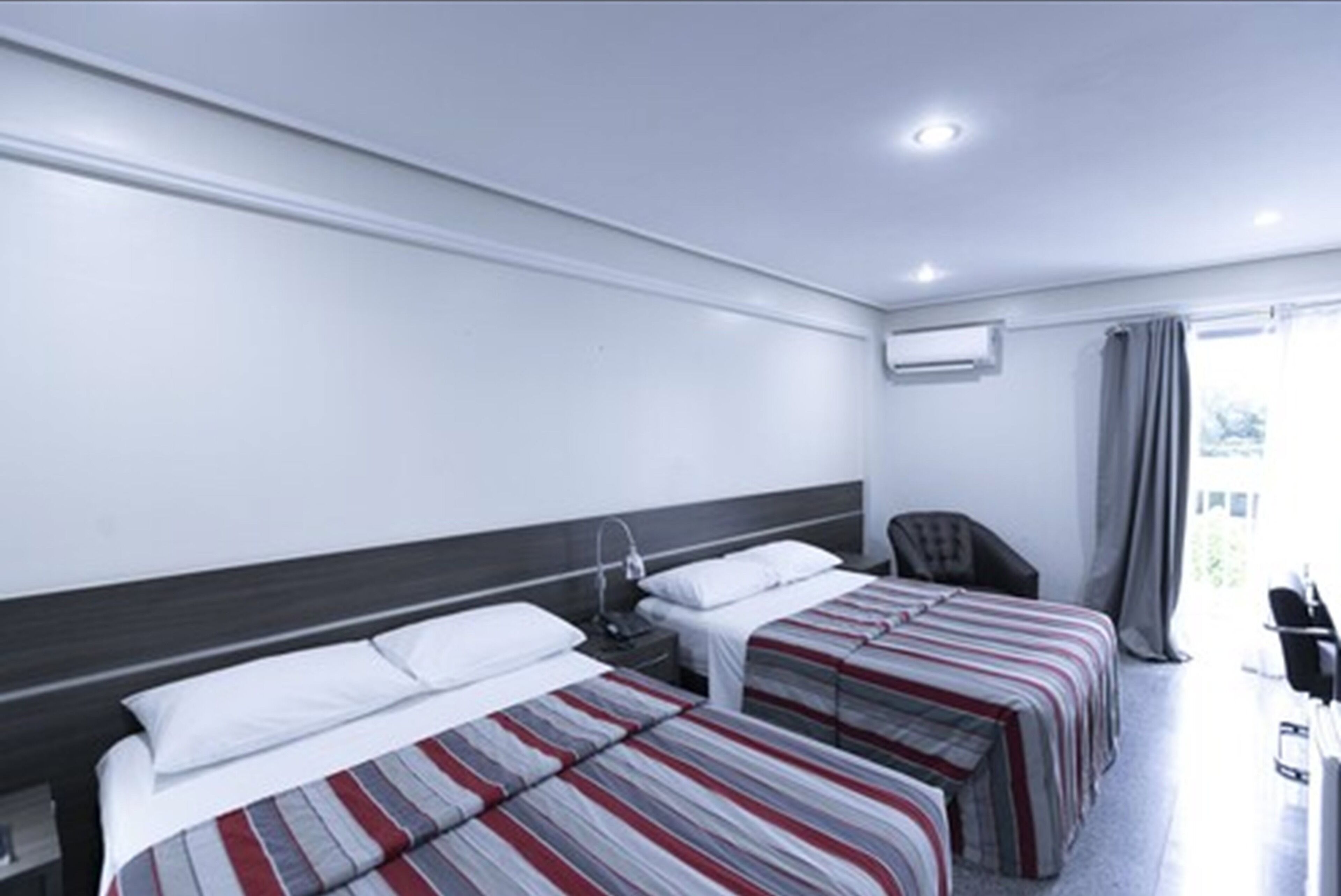 A hotel room with two beds, a desk, a chair, and a window with curtains.