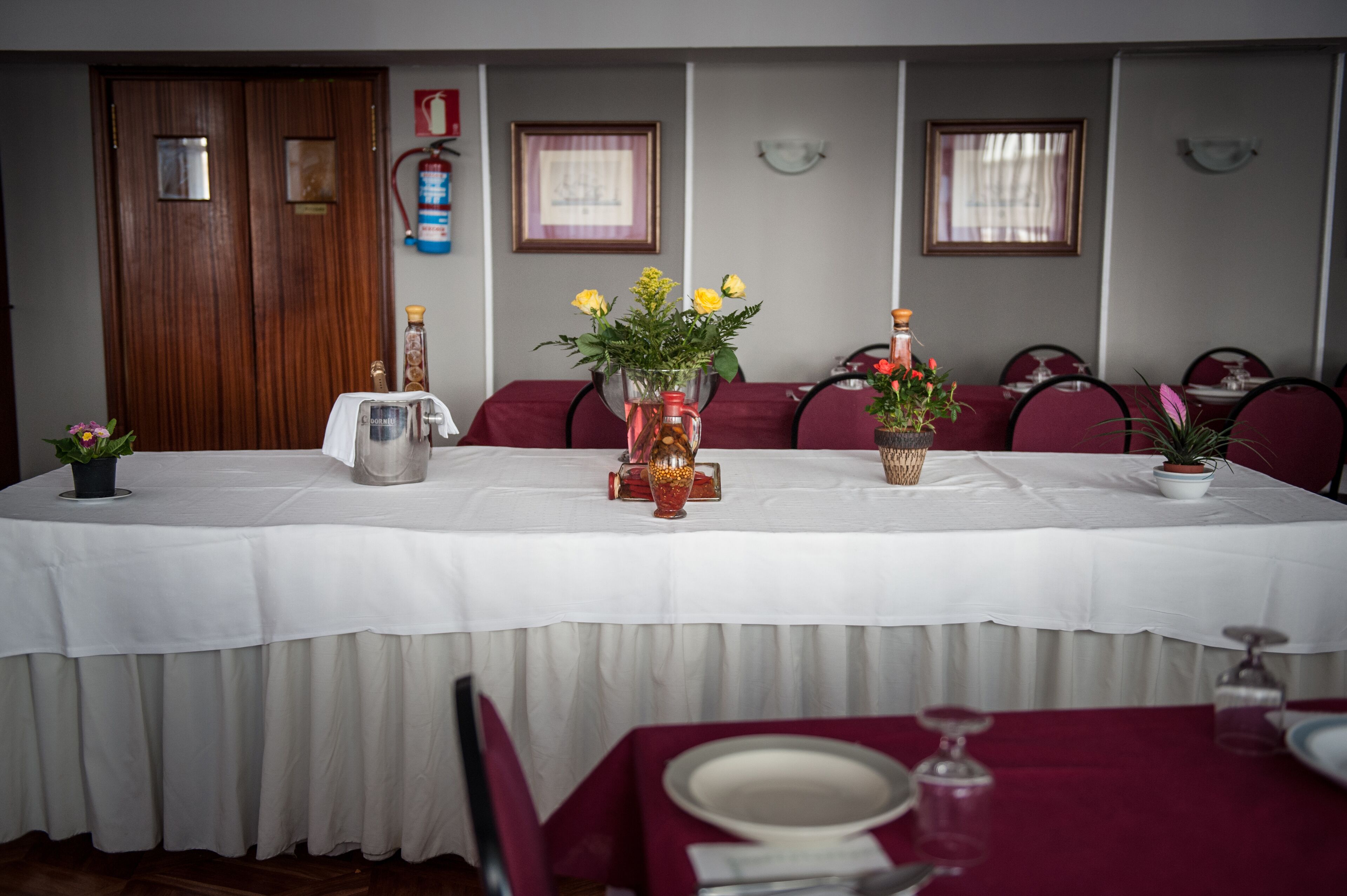 Una mesa de comedor con manteles blancos, sillas rojas y centros de mesa florales.