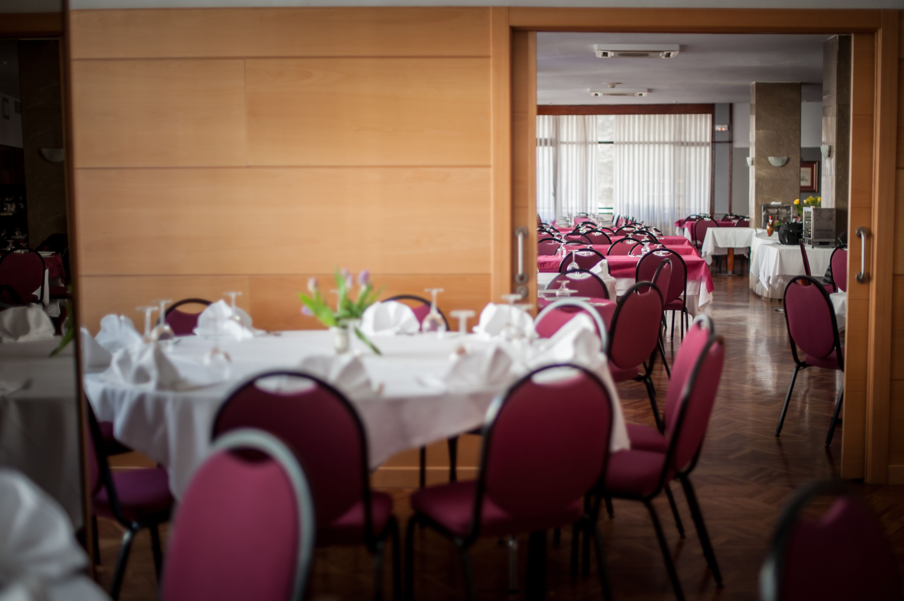 A dining area with tables set for multiple guests, featuring red chairs and white tablecloths.