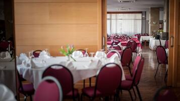 A dining area with tables set for multiple guests, featuring red chairs and white tablecloths.