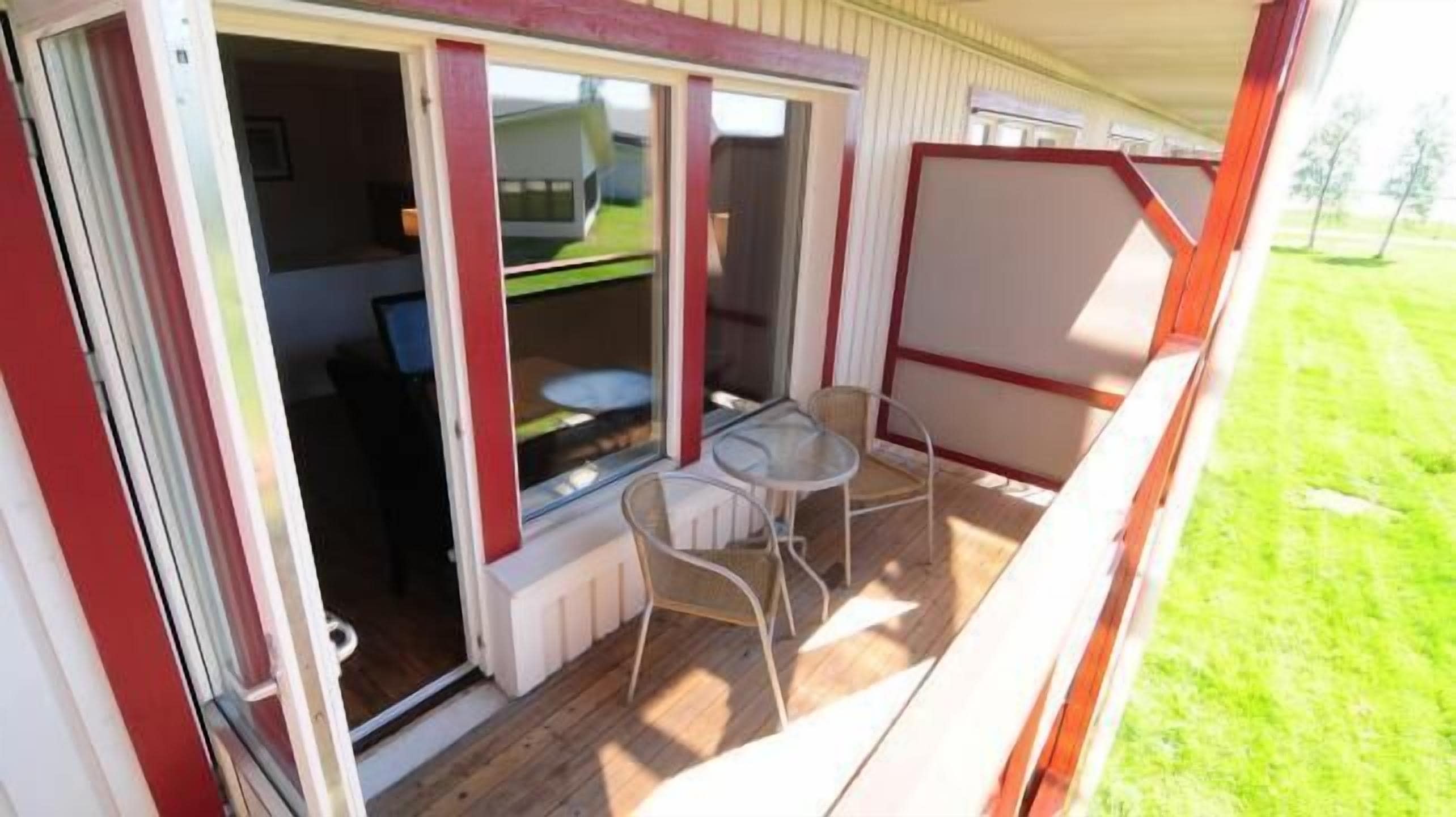 Un espacio al aire libre techado con una mesa, sillas, una ventana y una puerta que da al interior.