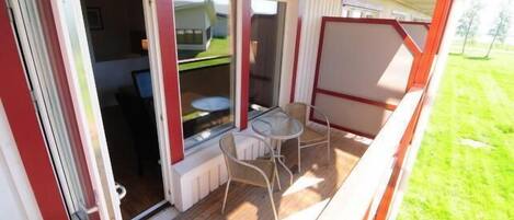 Un espacio al aire libre techado con una mesa, sillas, una ventana y una puerta que da al interior.
