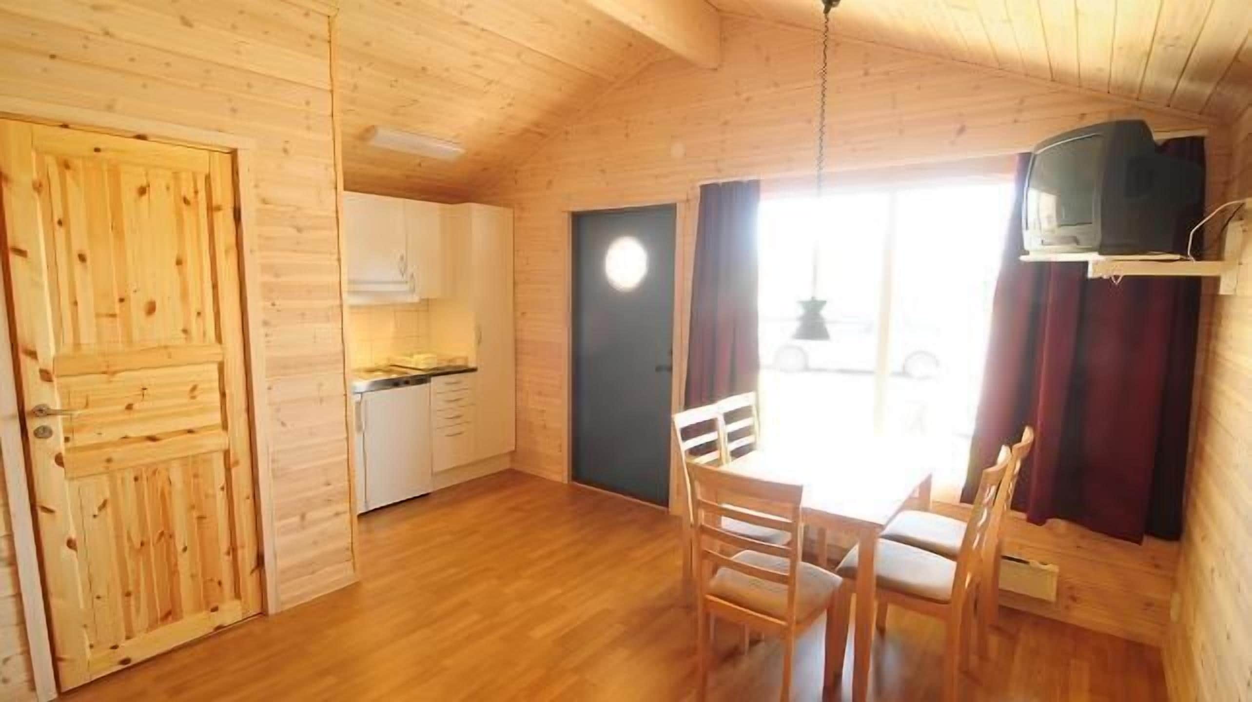 A small wooden cabin with a kitchen, dining area, and a single TV.