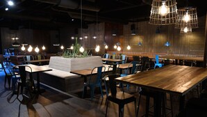 A restaurant interior with wooden tables and chairs, a central planter with plants, and hanging light fixtures. - Pite Havsbad (Pitea)