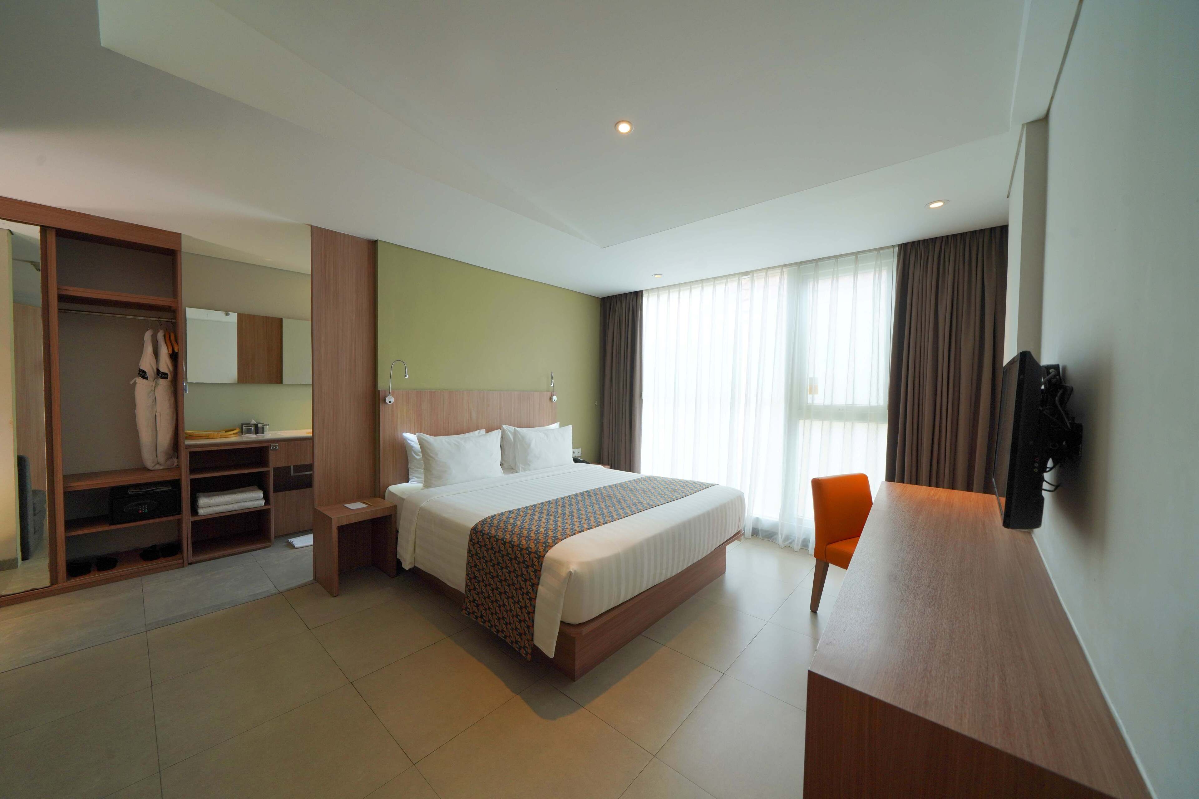 A hotel room with a large bed, a wooden desk, a chair, a wardrobe, and a television.