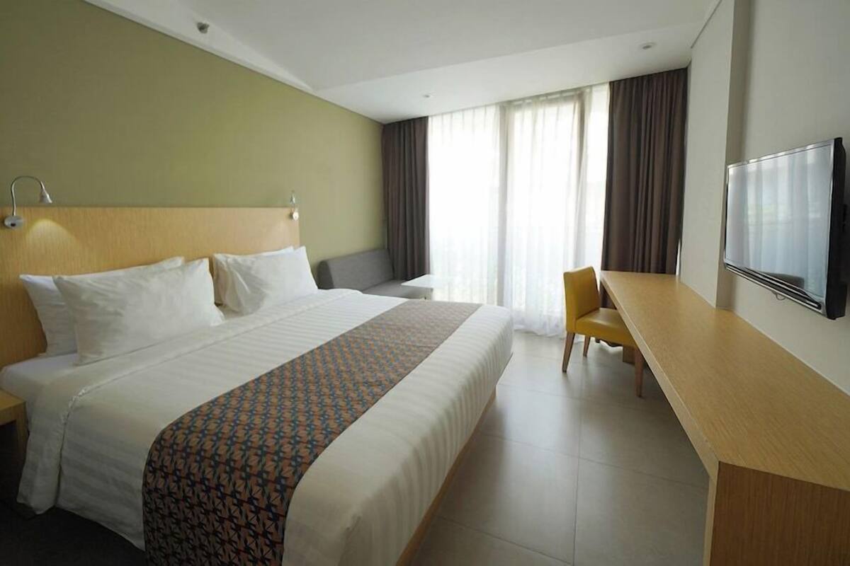 Une chambre d’hôtel avec un grand lit, un bureau, une chaise, une télévision et des rideaux.