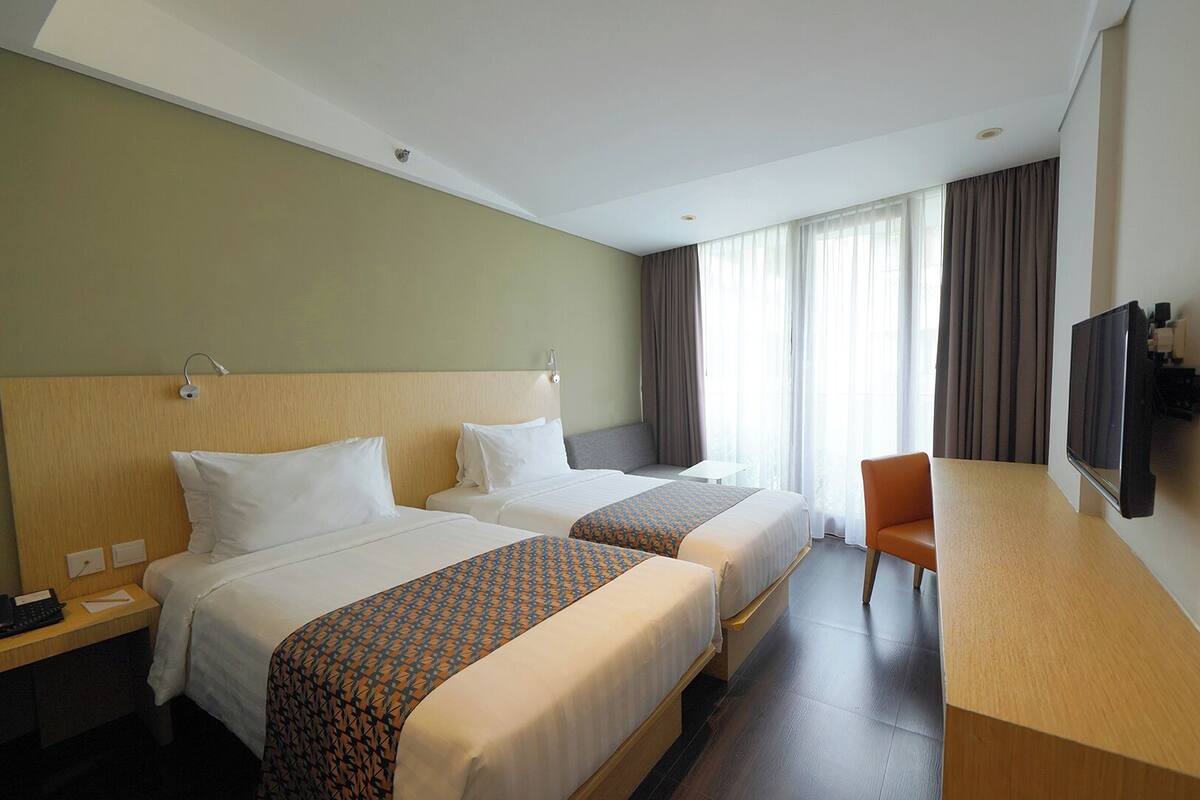 Une chambre d’hôtel avec deux lits, un bureau, une chaise, une télévision et une fenêtre avec des rideaux.