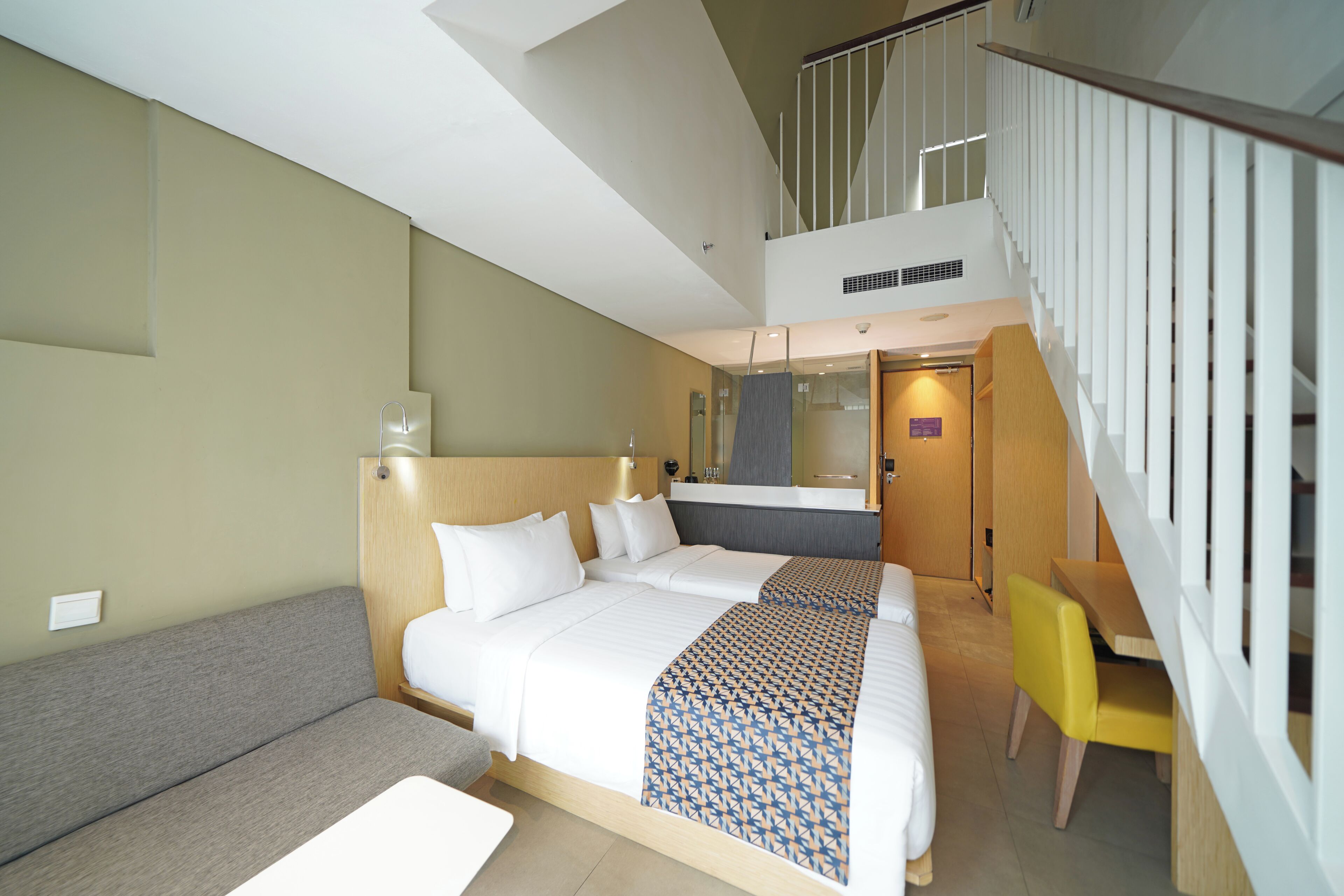A hotel room with a large bed, a sofa, a desk, and a staircase.