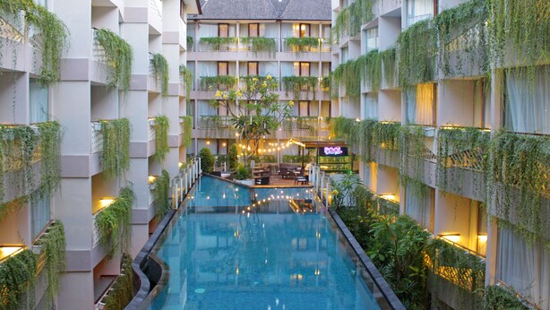 A hotel with a central pool, multiple balconies with greenery, and a bar area. - Episode Kuta Bali (Kuta)