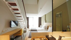 A modern hotel room with a bed, desk, chair, television, and a bathroom with a mirror and sink. - Episode Kuta Bali (Kuta)