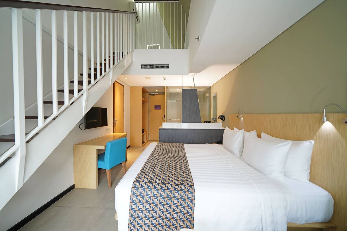 Une chambre d’hôtel avec un lit, un bureau, une chaise, une télévision et un escalier.
