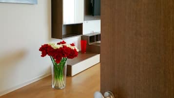A modern living room with a wooden floor, a glass vase with red and white flowers, a red cup, and a flat-screen TV on a wooden shelf.