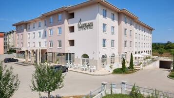 Ein mehrstöckiges Hotel mit modernem Design, das einen zentralen Innenhof mit Außenbestuhlung und einem überdachten Bereich bietet.