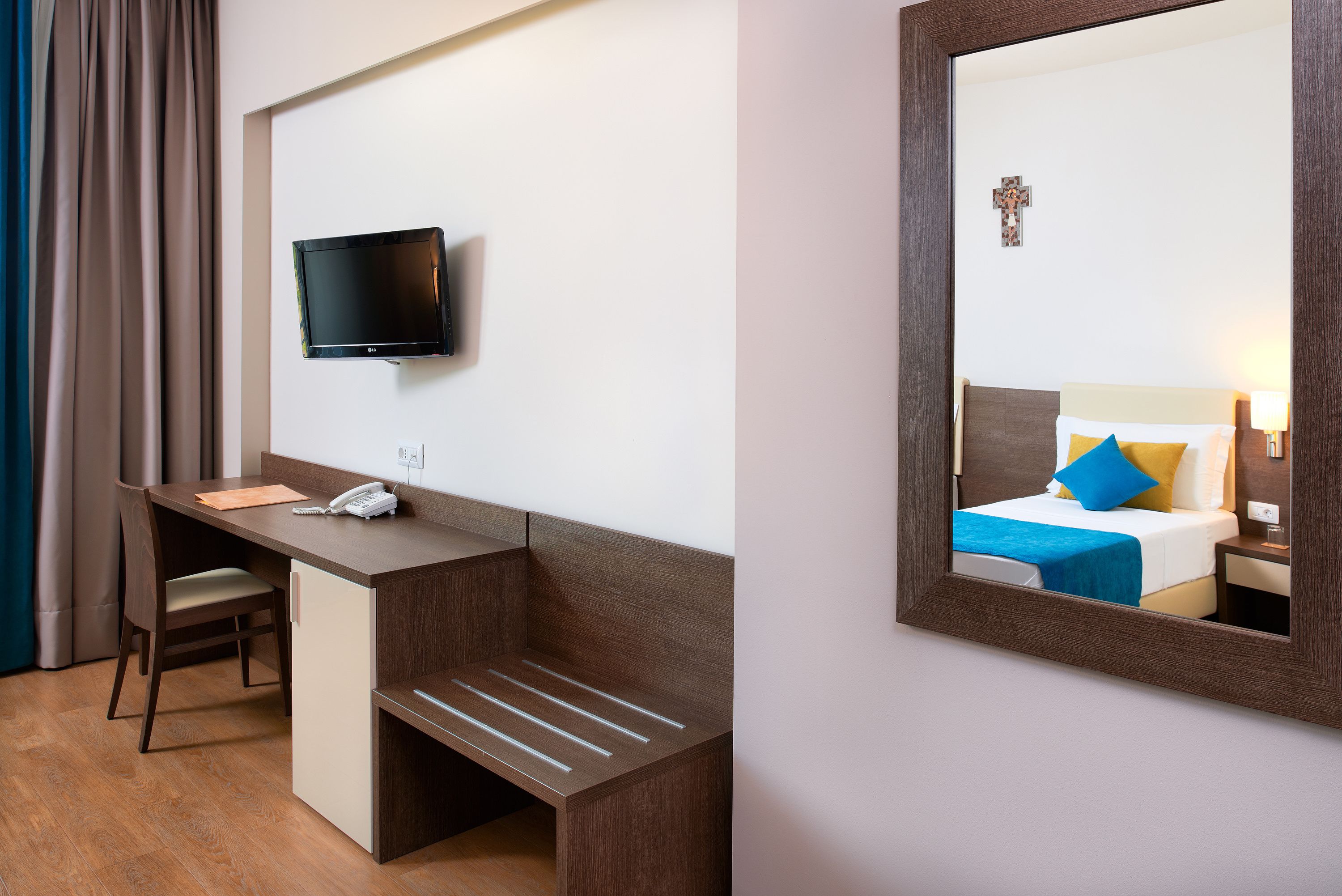 Hotelkamer met bureau, stoel, televisie en een bed met blauw kussen.