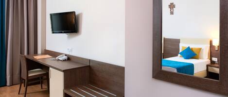 Hotelkamer met bureau, stoel, televisie en een bed met blauw kussen.