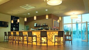 A bar area with a curved counter, multiple bar stools, and a view through large windows. - Medjugorje Hotel & Spa (Citluk)