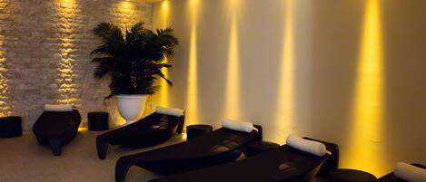 A spa area with massage chairs, a large potted plant, and a textured stone wall.