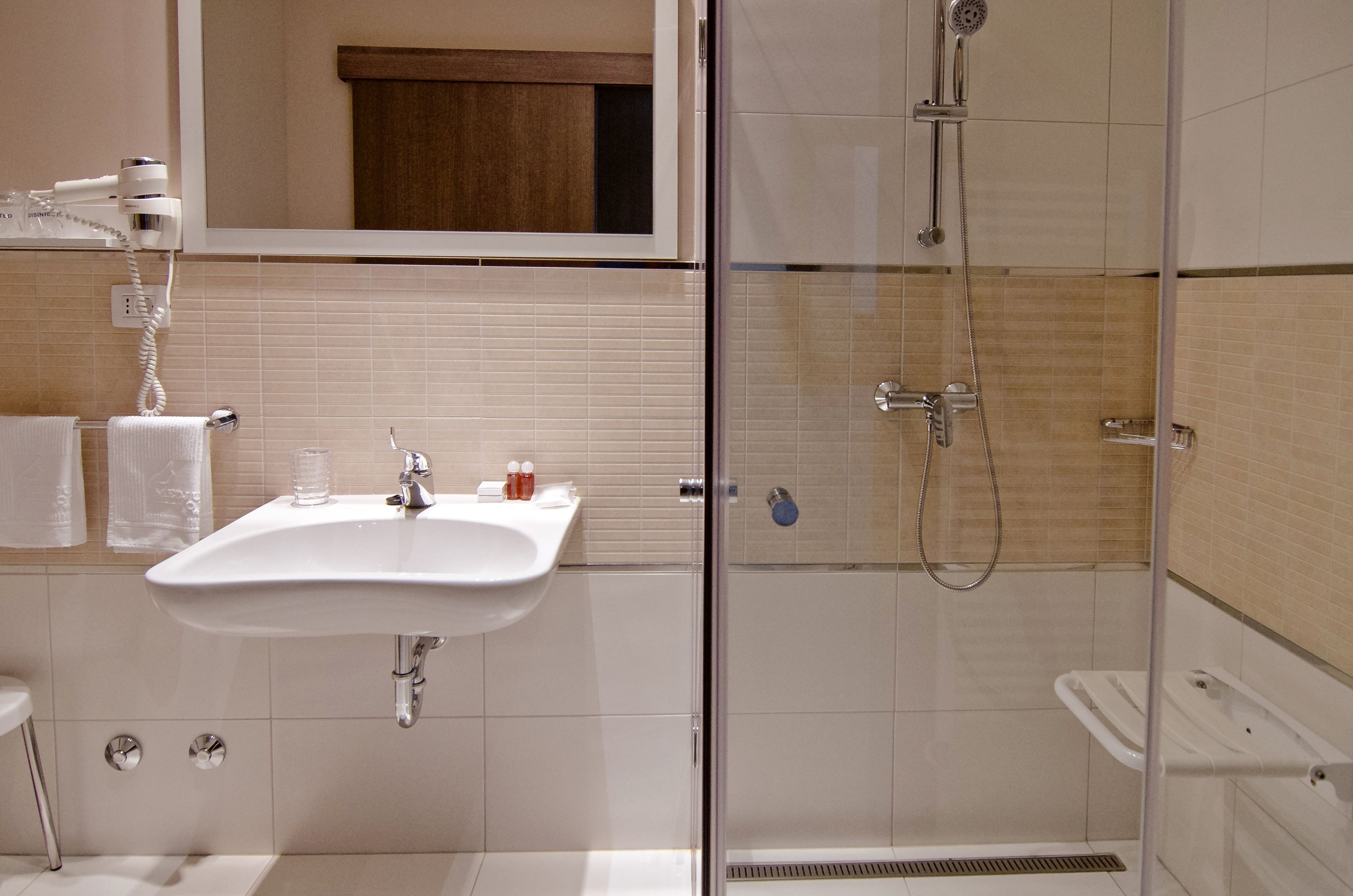 Un baño con lavamanos, espejo y ducha con mampara de vidrio.