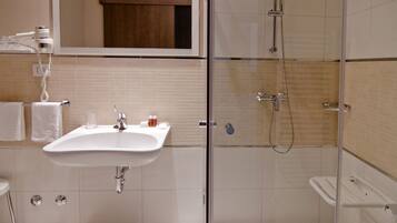 Un baño con lavamanos, espejo y ducha con mampara de vidrio.