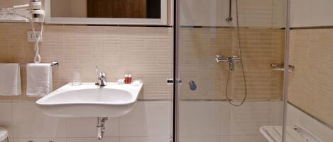 Un baño con lavamanos, espejo y ducha con mampara de vidrio.
