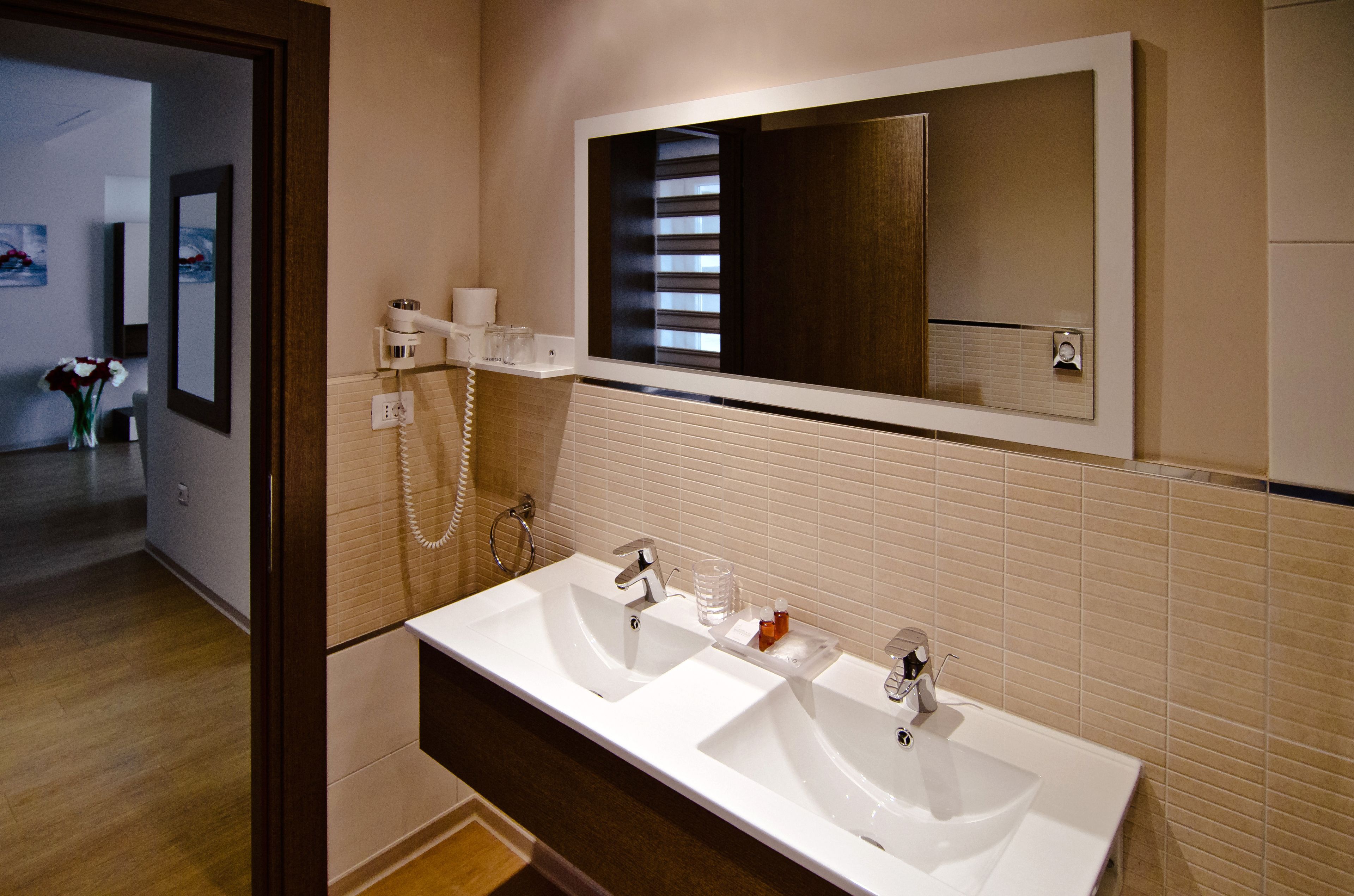 Ein modernes Badezimmer mit zwei Waschbecken, einem großen Spiegel und einem Föhn an der Wand.