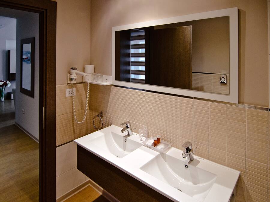 Une salle de bain moderne avec deux lavabos, un grand miroir et un sèche-cheveux fixé au mur.