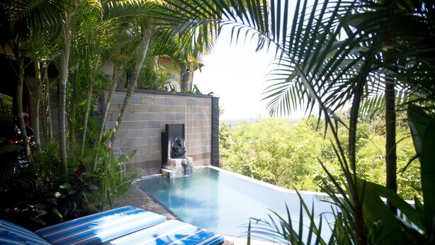 An infinity pool with lounge chairs, surrounded by lush greenery and a stone wall. - Jimbaran Cliffs Private Pool Hotel & Spa (Nusa Dua)
