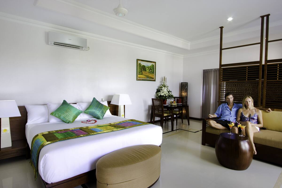 A hotel room with a bed, a sofa, a dining table, and a decorative plant.