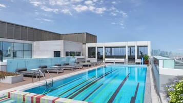 A rooftop swimming pool with lounge chairs, a city view, and a modern building in the background.