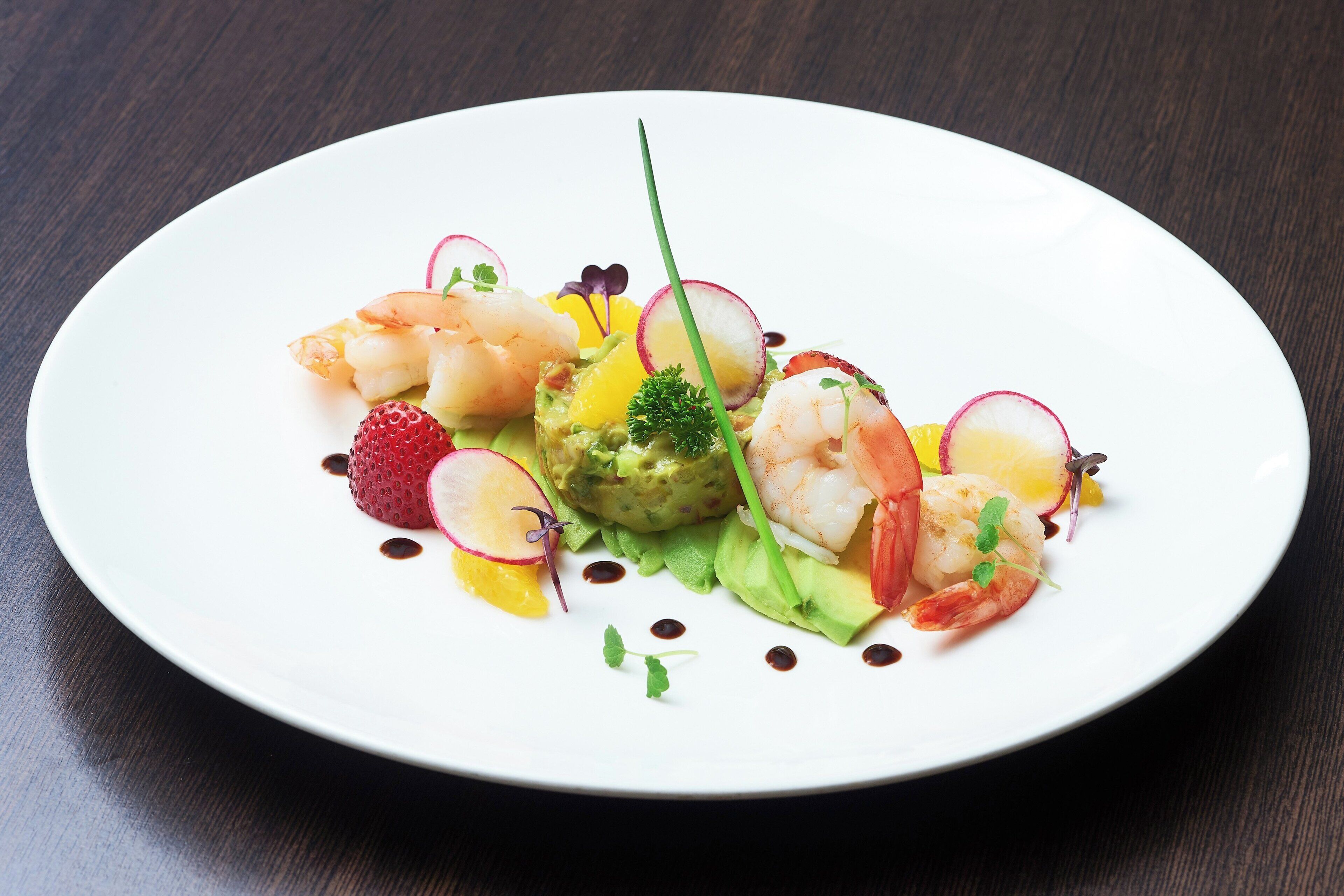 A white plate with a seafood dish, including shrimp and avocado, on a dark wooden table.