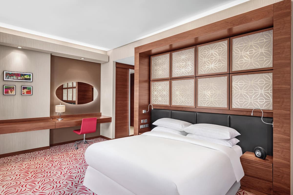 A hotel room with a large bed, a desk with a chair, a mirror, and a wall with decorative panels.