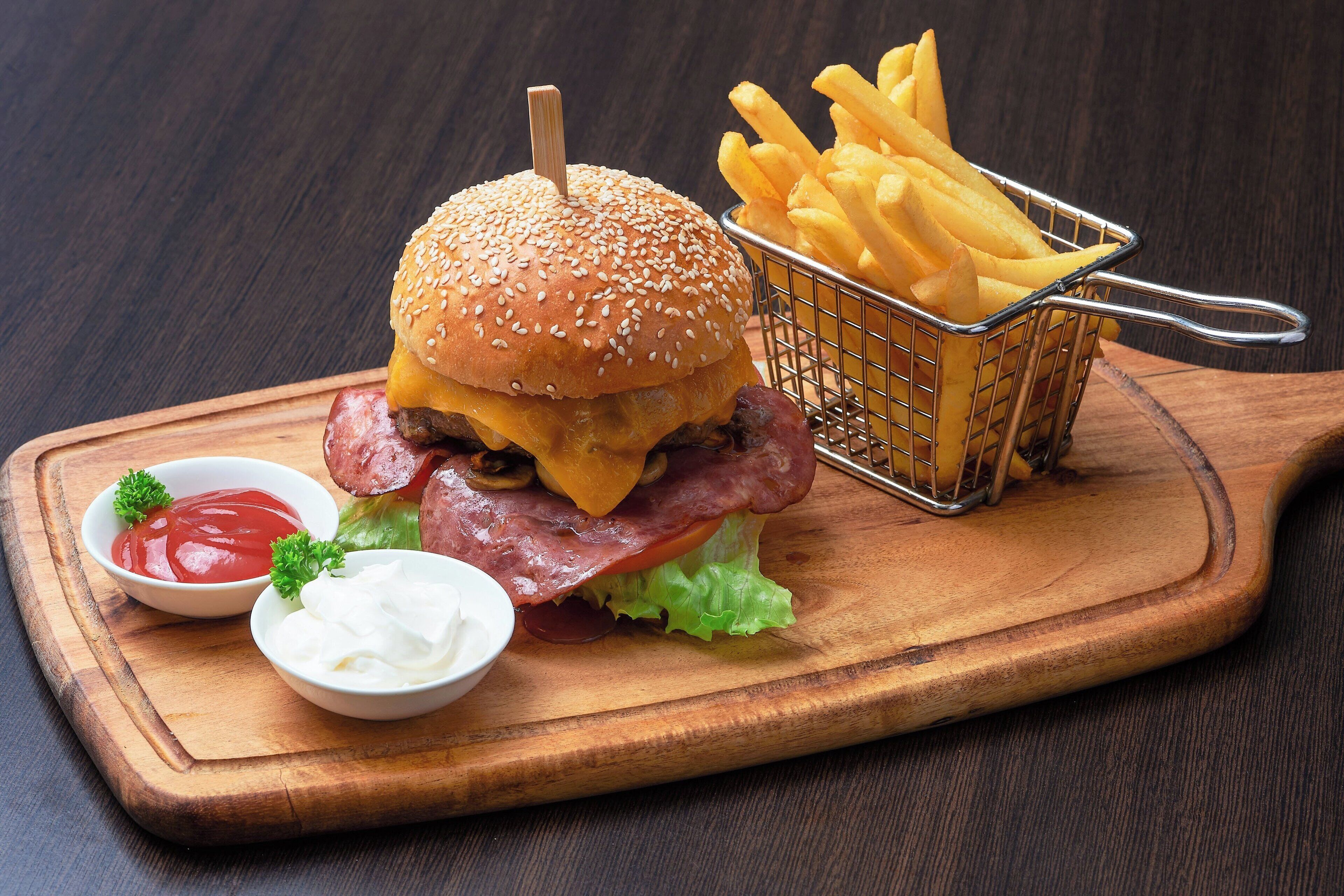 Hamburguesa con papas fritas y aderezos sobre una tabla de madera.
