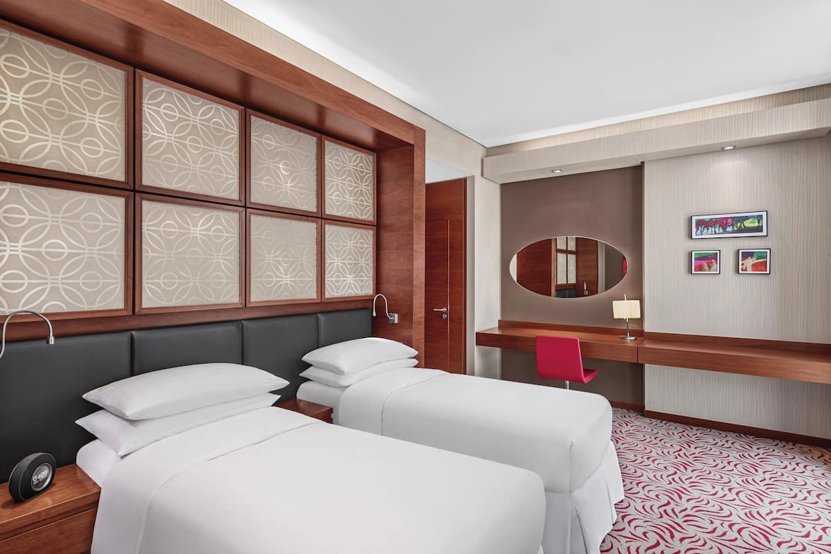 A hotel room with two beds, a vanity with a mirror, and a red chair.