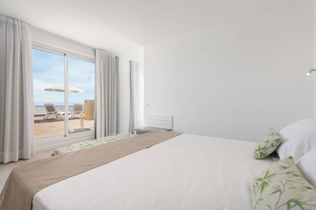 A hotel room with a large bed, a view of the beach, and a balcony with chairs and an umbrella.