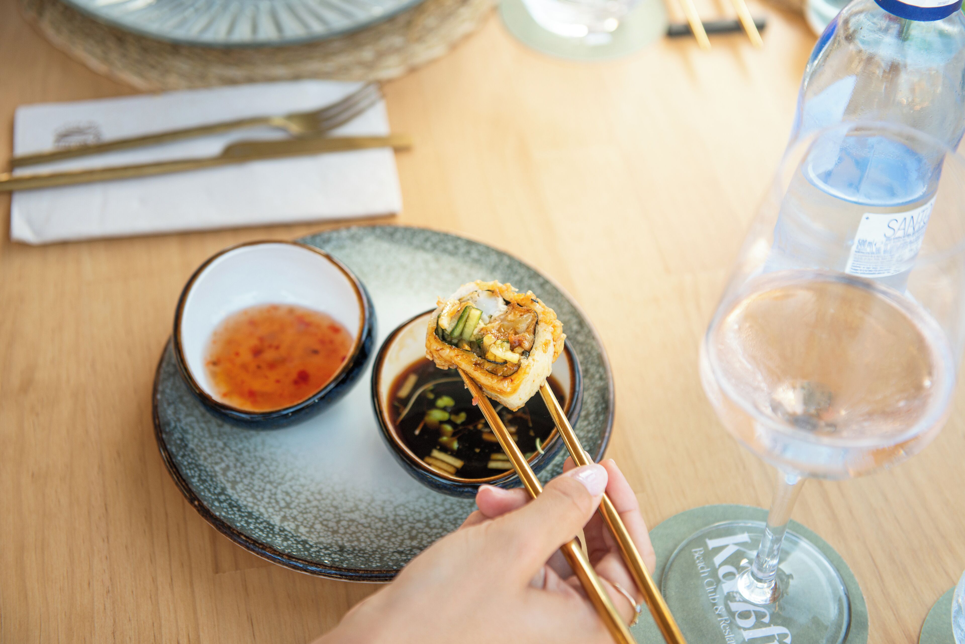 A dining table with a plate of sushi, a bowl of dipping sauce, and a bottle of water.