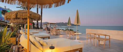 A beachside lounge with sunbeds, a table, and chairs, overlooking the sea.