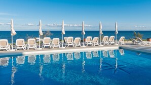 Zona de piscina amb gandules i ombrelles, amb vista a un mar blau i tranquil.