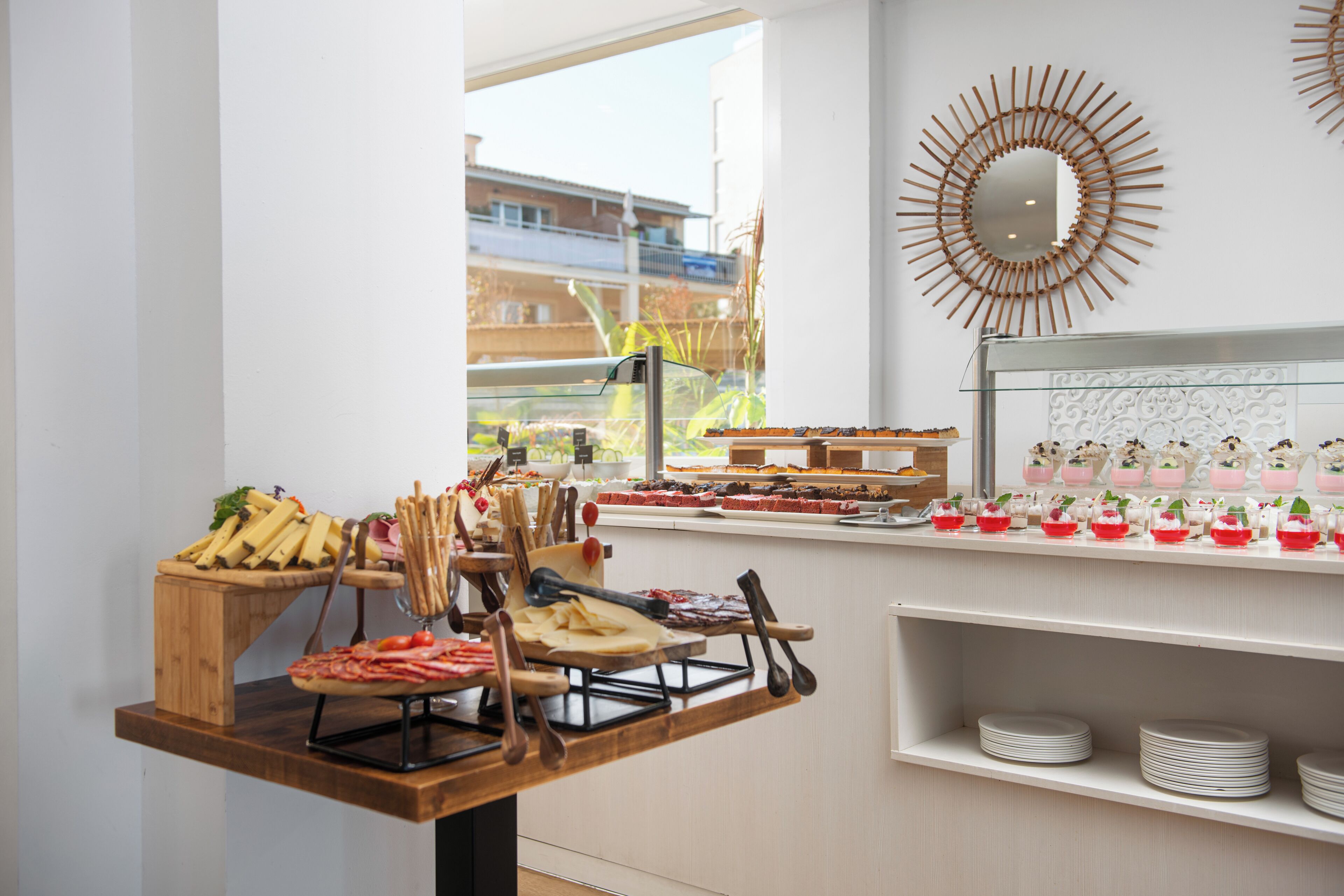 A buffet setup with various food items and utensils, a decorative mirror, and a view of buildings outside.