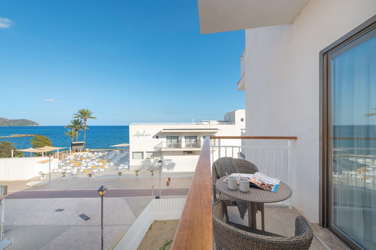 A balcony with a view of the sea, wicker furniture, and a building labeled "Atelier" in the background.