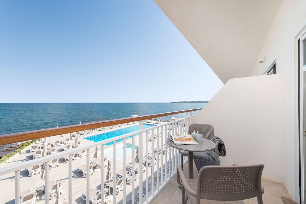 A balcony with a pool, lounge chairs, and a table with a book and a cup.