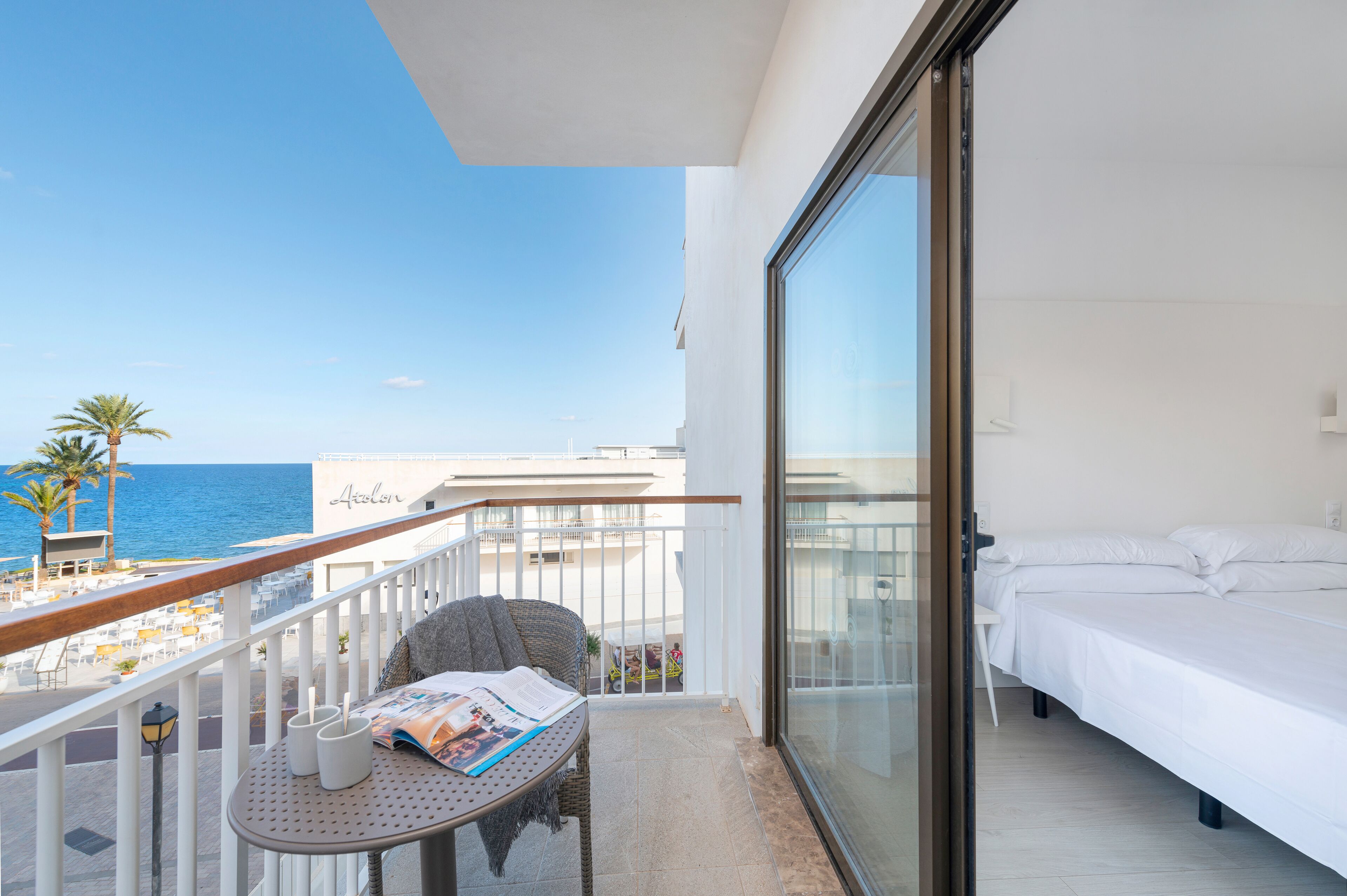 Un balcon avec vue sur la mer, un lit et une table avec des documents à lire.