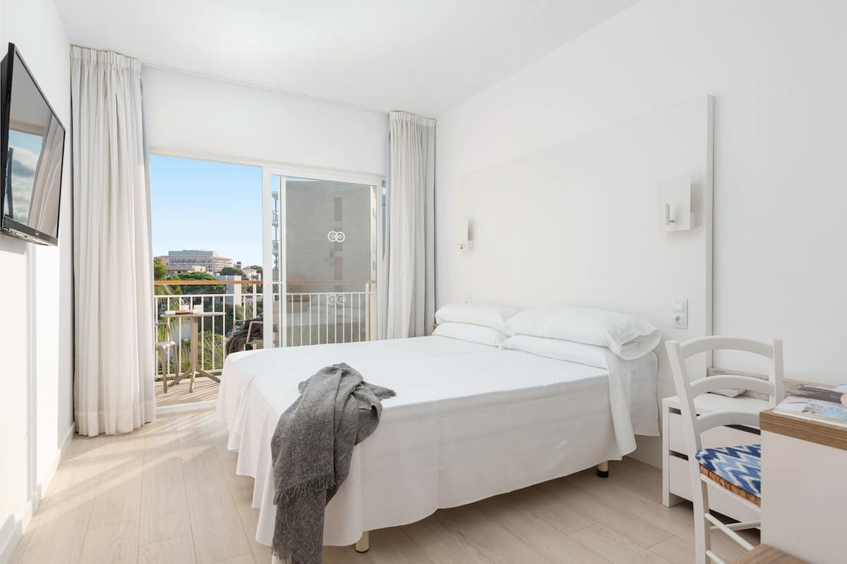 A bedroom with a bed, a chair, a table, and a balcony with curtains.